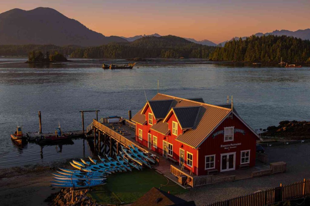 Rows of kayaks lined up outside a waterfront rental shop with mountains and golden sunset in the background