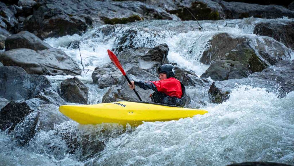 Kayaker wearing a black helmet paddling through rapids tightly surrounded by large rocks