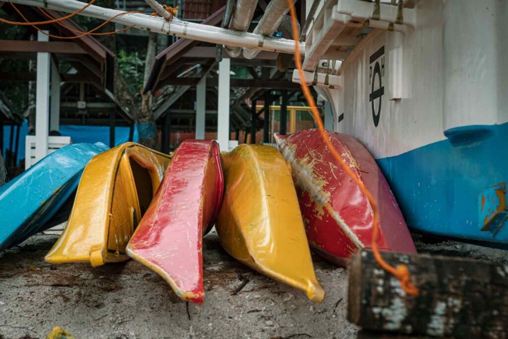 Blue, yellow, and red kayaks stacked and stored together beside a building, showing how kayaks are kept between trips