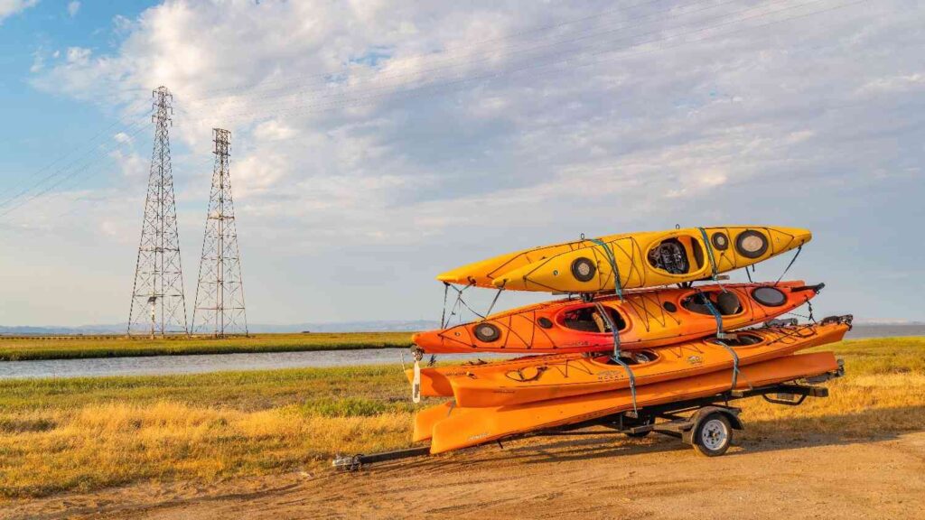 Three fishing kayaks stacked and strapped onto a trailer, ready for transport