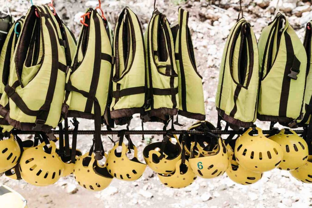 Multiple life jackets and helmets hang together, ready to be worn before a kayak launch