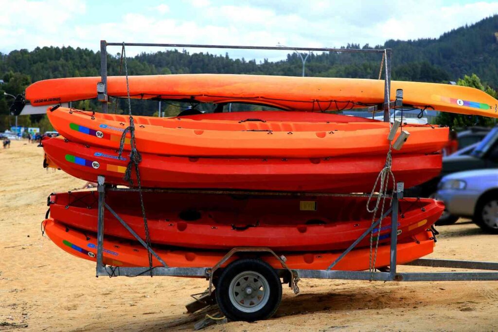 Multiple heavy kayaks stacked on a small trailer with a single wheel, illustrating the risk of overloading lightweight equipment