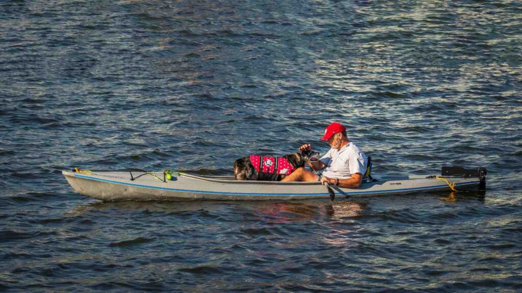 Man affectionately petting his dog's face while both sit together in a kayak at golden hour