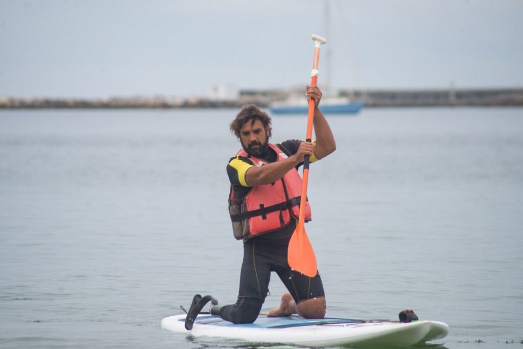 Man kneeling on a paddleboard wearing a life vest while paddling on calm open water