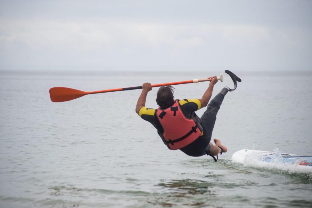 Man falling off a paddleboard mid-air while holding the paddle above the water