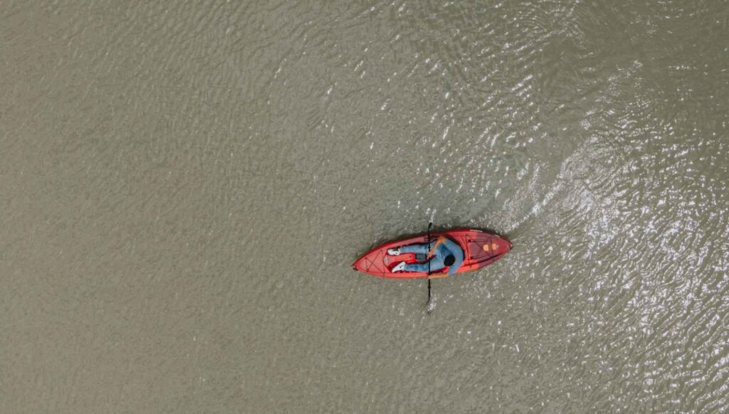 An aerial view of a paddler leaning down into a red kayak while adjusting their position on the water