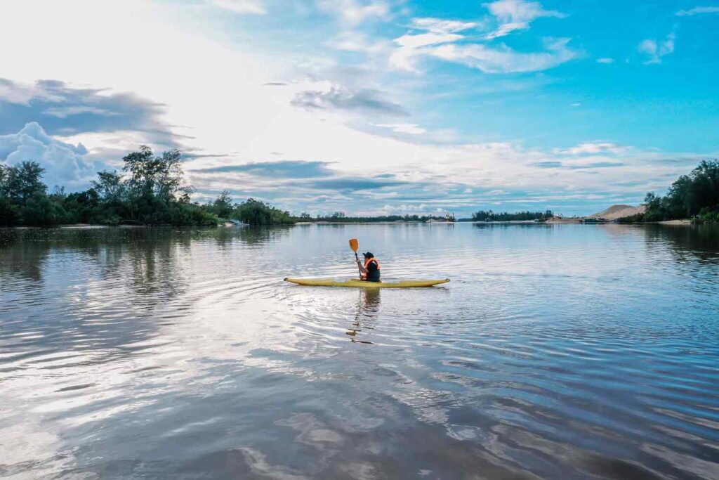 Solo kayaker paddling a sit-inside kayak across a wide open lake under a blue sky
