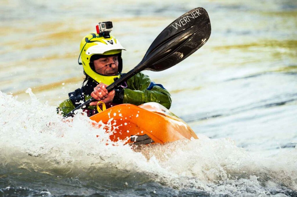 Close-up of a paddler wearing a bright yellow kayak-specific helmet with camera mount while navigating splashing water