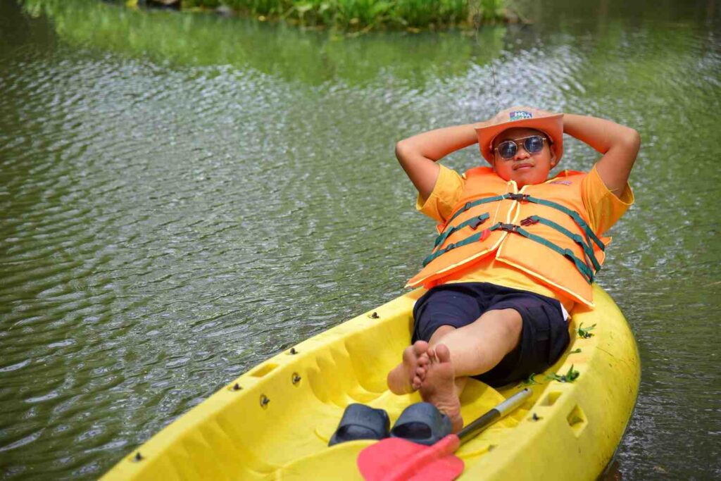 A paddler leans back completely relaxed in a yellow kayak on calm green water