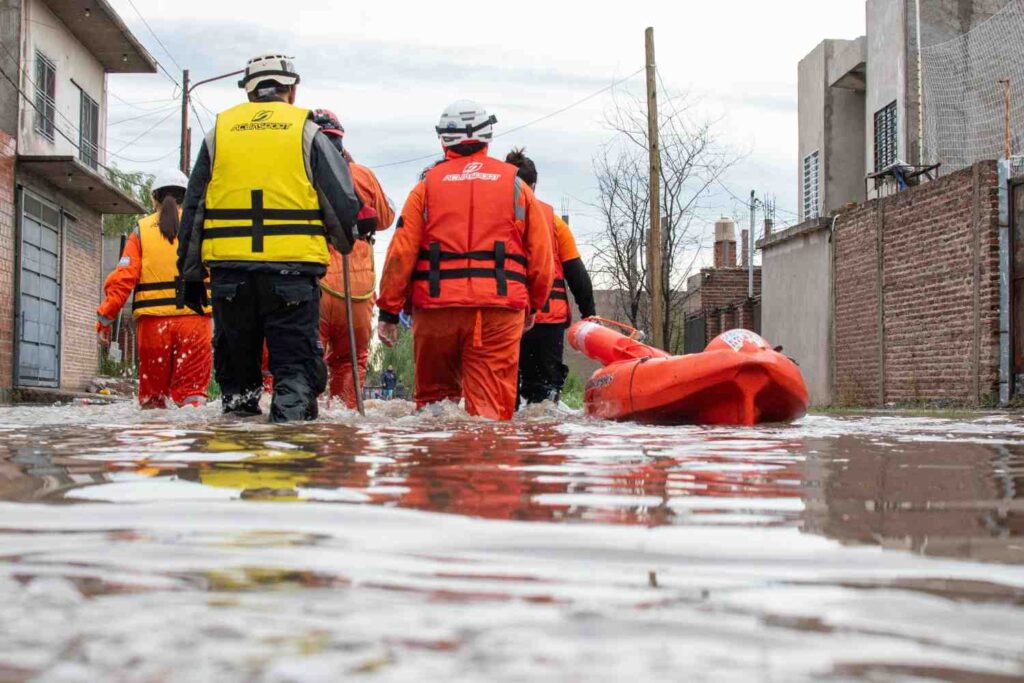 A team wearing life jackets and helmets moves a rescue kayak through flooded water together