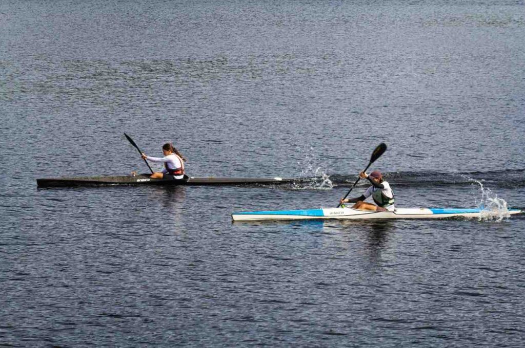 Two paddlers racing in narrow, streamlined kayaks demonstrating speed and efficient paddling