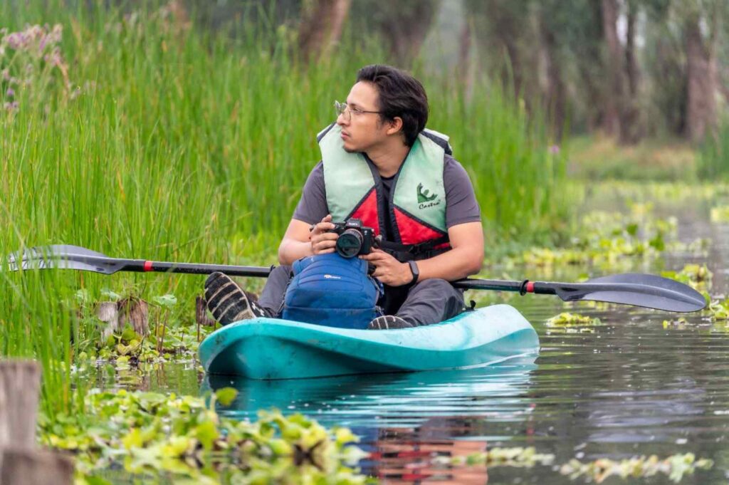 Man wearing a life jacket sitting comfortably on an open sit-on-top kayak surrounded by reeds
