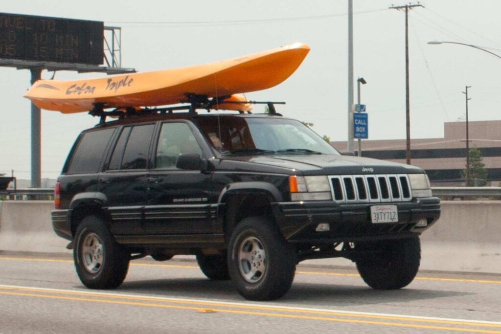 Jeep Grand Cherokee SUV driving on the highway with a kayak securely mounted on its roof rack
