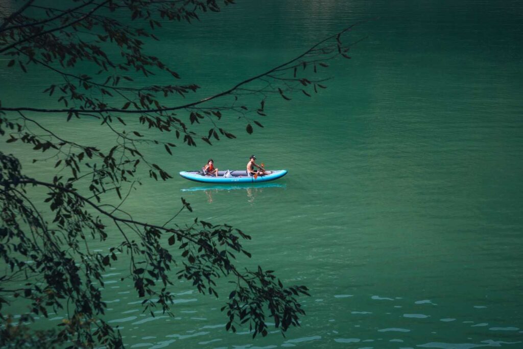 Two people paddling a tandem inflatable kayak on calm turquoise lake water surrounded by trees