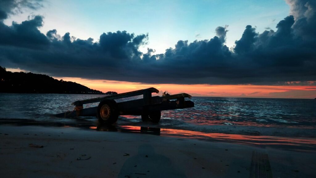An empty wheeled cart frame silhouetted against the water at sunset