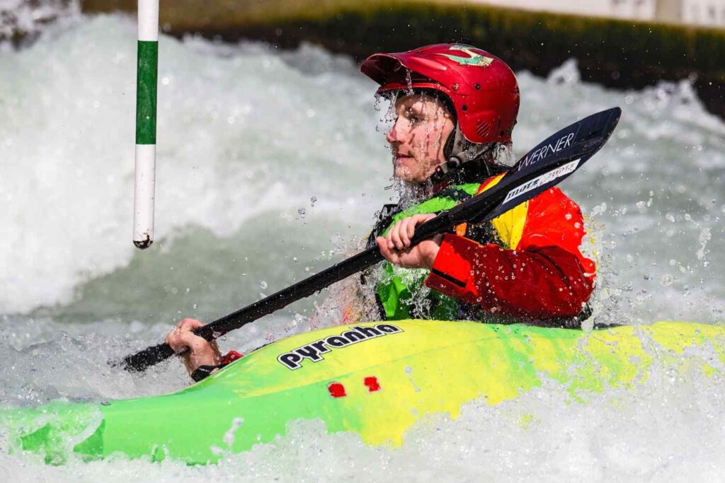 Close-up of a kayaker wearing a red helmet while paddling through whitewater slalom rapids