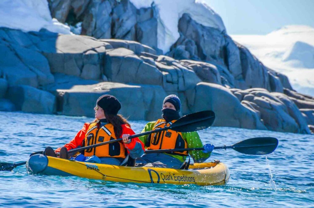 Kayakers paddling in icy polar waters, gloved hands visible while gripping the paddle near glaciers