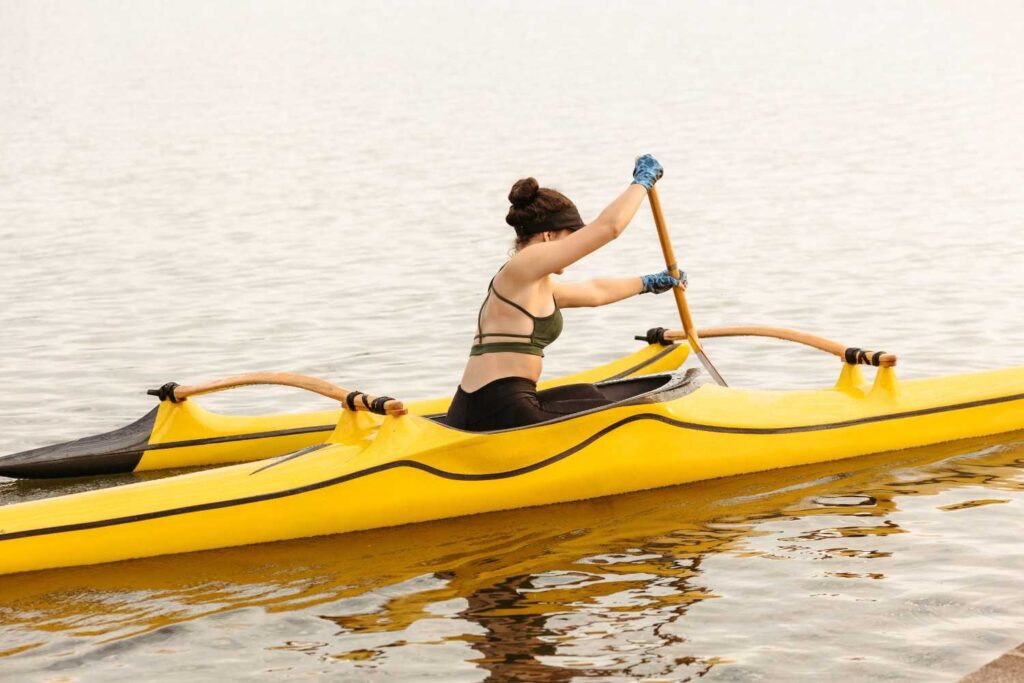 Paddler wearing blue gloves while paddling an outrigger canoe, hands fully covered on the paddle shaft