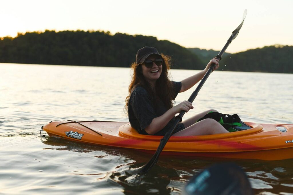 Smiling woman paddling a kayak on calm water wearing a life jacket