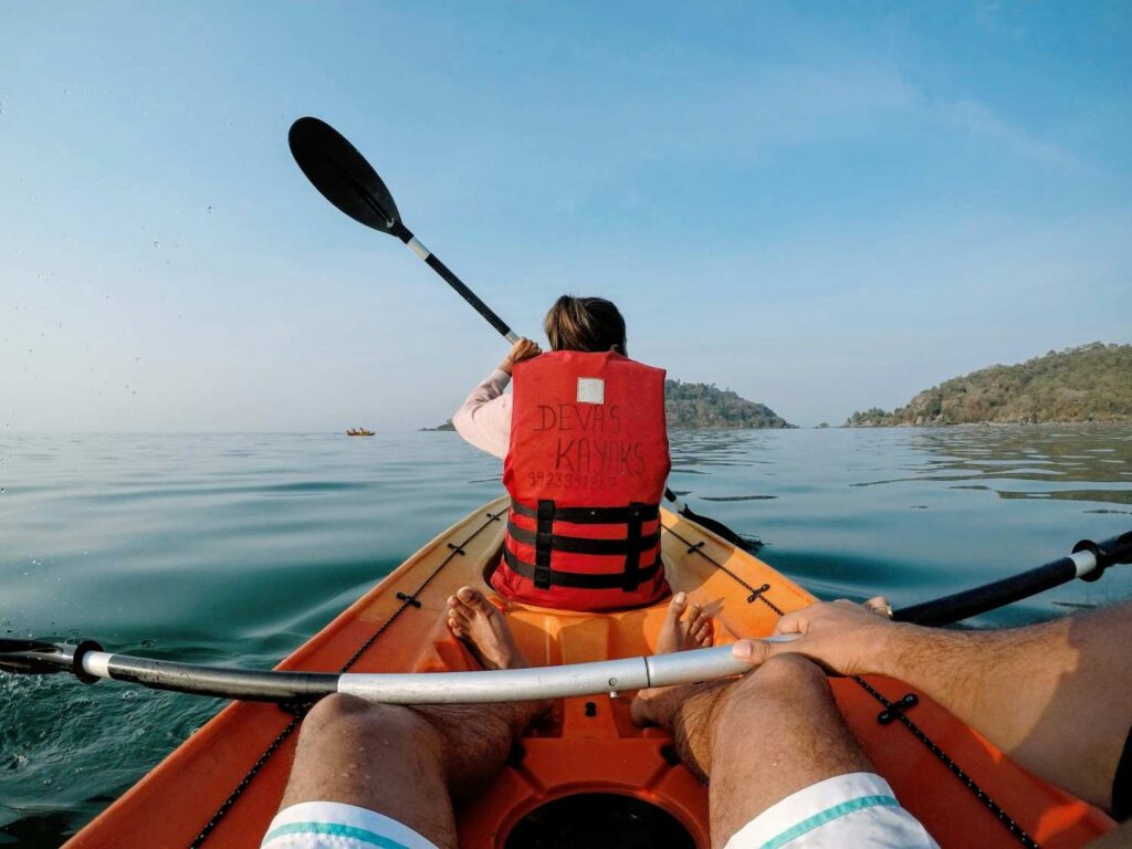 Two adults kayaking together on calm water, one wearing a red life jacket