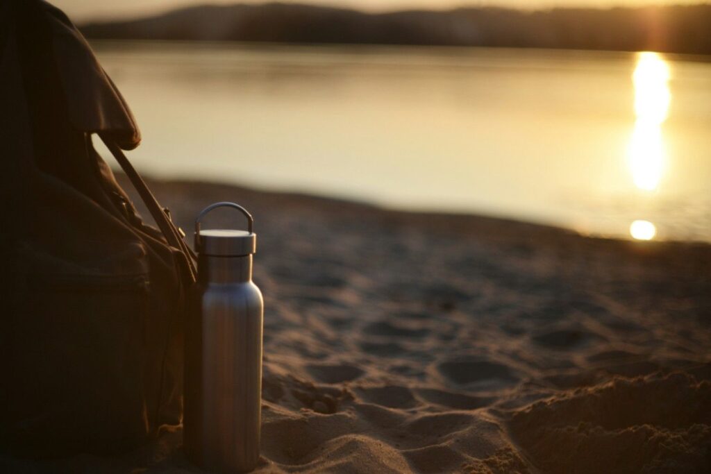 Water bottle and backpack on the beach at sunset for a kayaking trip